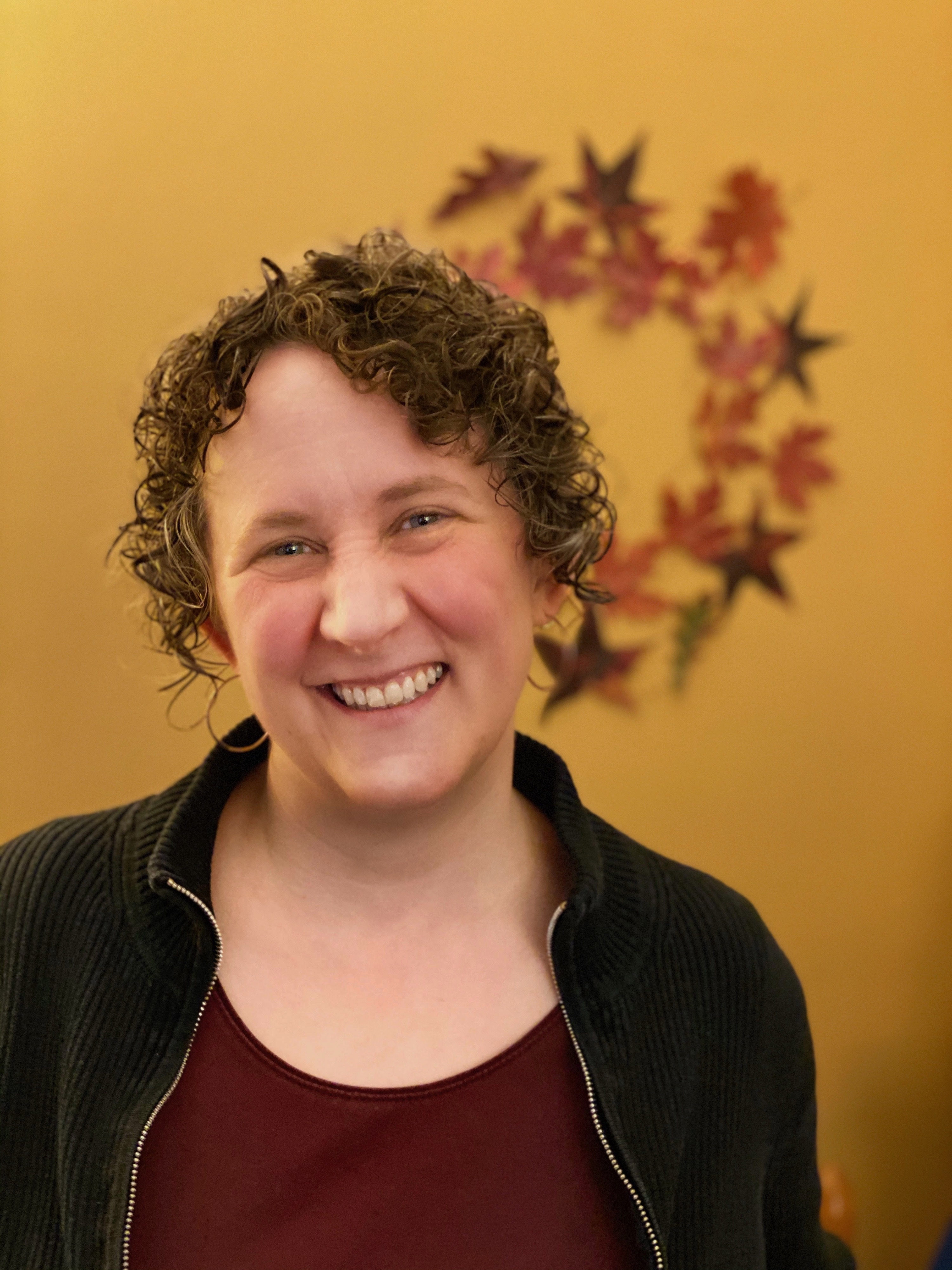 A woman with curly brown hair is smiling at the camera